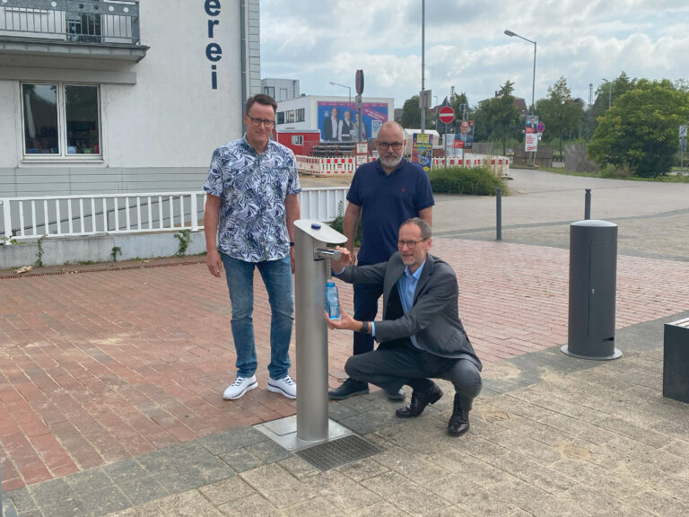 Bürgermeister Bernd Poggemöller, Betriebsleiter Matthias Kreft und Thorsten Held, Teamleiter Wasserversorgung, nehmen den Trinkwasserspender am Findeisen-Platz in Betrieb.