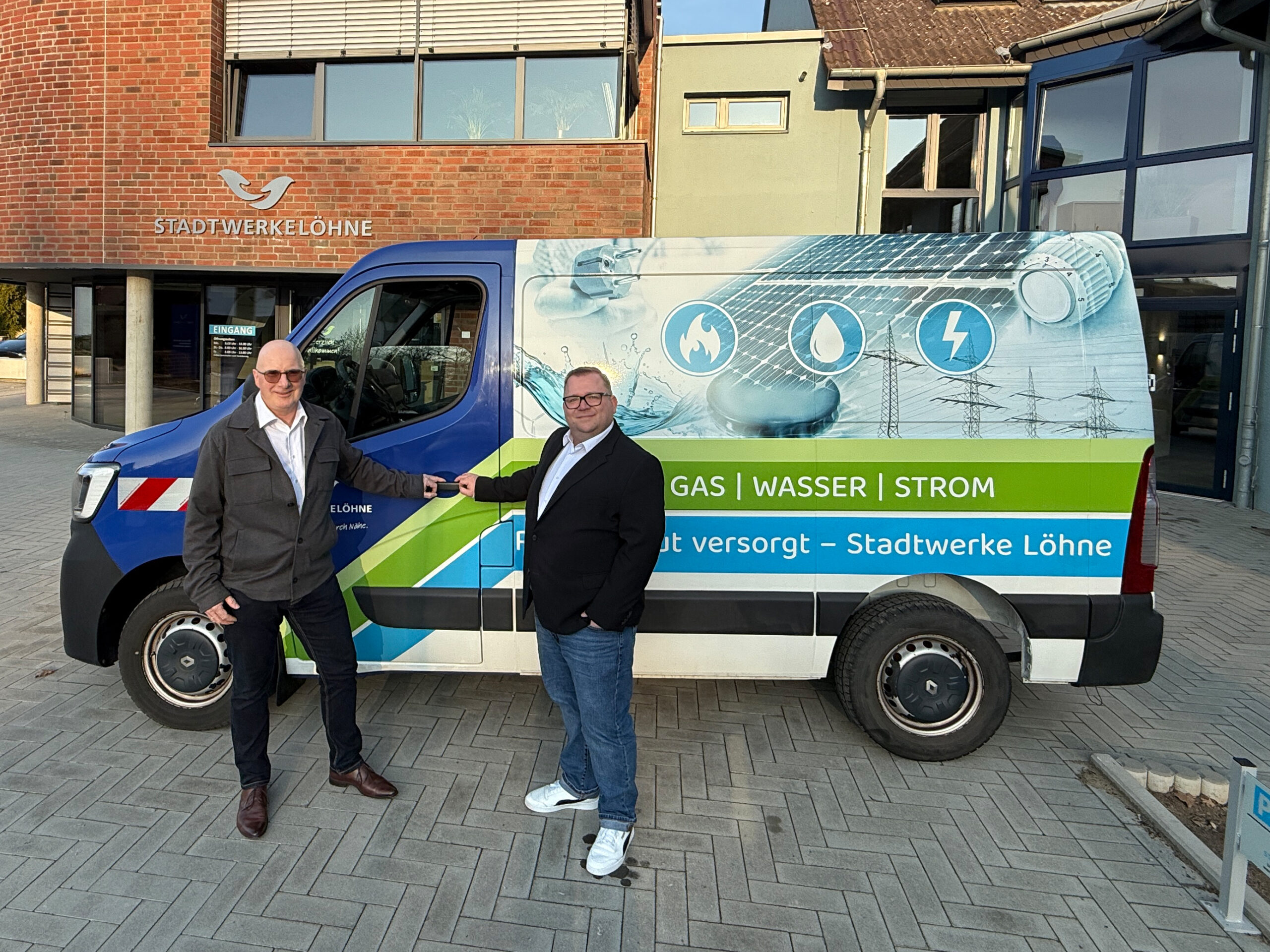 Die Betriebsleiter stehen vor dem Eingang mit einem Fahrzeug der Stadtwerke.