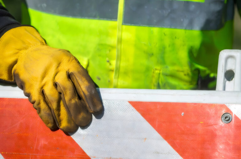 Person mit Warnweste und Handschuh hält Warnschild.