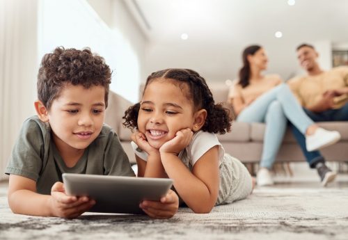 Learning, tablet and children streaming a video on technology on the living room floor of their house. Education, happiness and movies on technology for kids with parents on the sofa in their home.